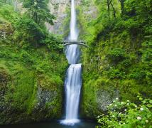 Walking bridge over a double waterfall surrounded by lush green mountain side