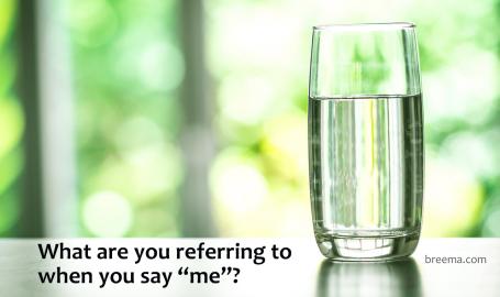 A glass of water on a table in front of a garden.