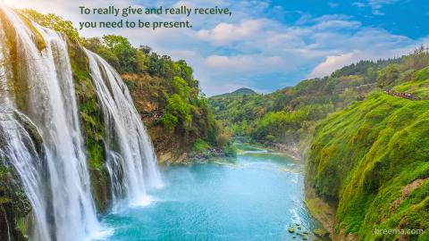 Multiple waterfalls over clear lake amidst lush green valley with sun cresting.