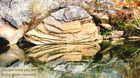 A rock reflecting on the surface of a still creek.