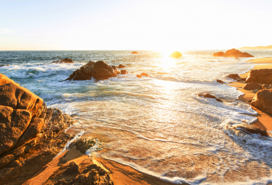 Tide coming up on rocky beach under the setting sun.